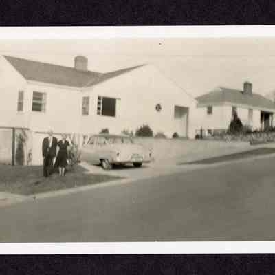 Two people standing near a row of houses on a paved street