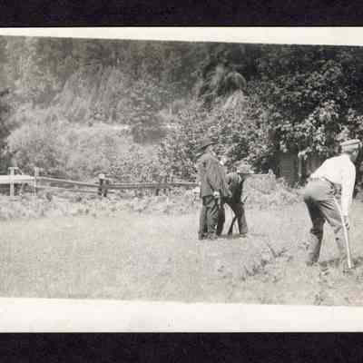 Photograph on postcard of three men in a field, from the lodge picnic at the Camp Creek School