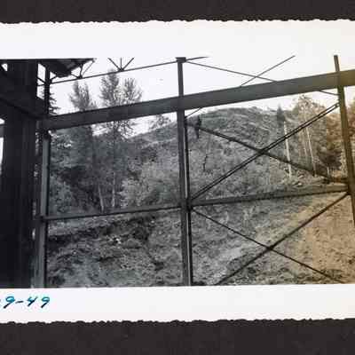 Photograph of the underside of a bridge or a large metal structure with a man on one of the beams, 1949
