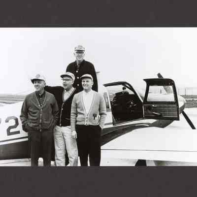 Photograph of four men standing outside an airplane