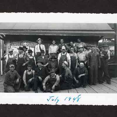 Photograph of a group of 25 unknown men infront of safety bulletin board at Booth-Kelly Lumber Mill