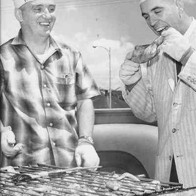 Photograph of two men in chef hats standing at the broiler rack, circa 1960s