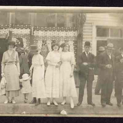Postcard, group of 4 women with a child, and 3 men, standing on sidewalk, undated