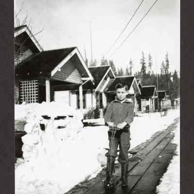 Photograph of boy riding scooter down snowy plank sidewalk, Wendling, Oregon