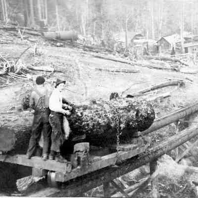 Photograph of two unidentified men next to logs on wooden tracks, Lane County, Oregon, 1935