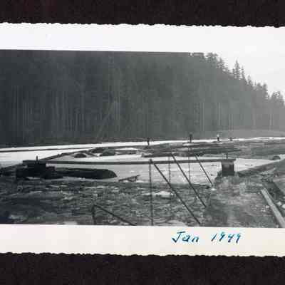 Photograph of four men on logs in a log pond