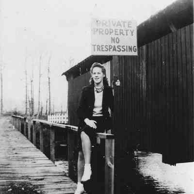 Photograph of a Woman sitting on fence next to a covered bridge, date unknown