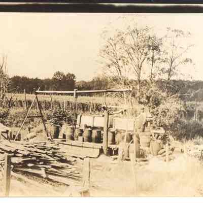 Photograph of an unknown man in a hop yard behind barrels