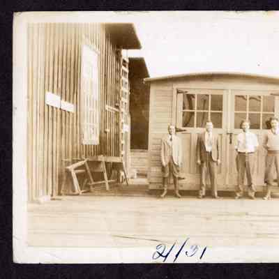 Photograph of four unknown men standing outside an unknown mill, 1931