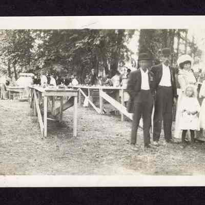Photograph on postcard of tables with food and people standing them