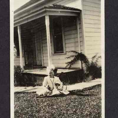 Photograph of a girl sitting in front of house with a doll, undated
