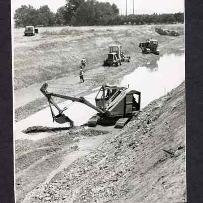 Photograph of construction work and equipment, digging section of field, 2 men, undated