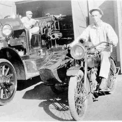 Photograph of unknown men on fire truck and motorcycle