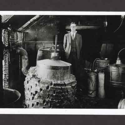 Photograph of Sheriff C.A. "Tom" Swartz Standing Behind Metal Cylinders/Stills, 1934