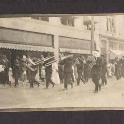 Photograph of a Post Cards of a parade with a brass marching band. Date unknown.