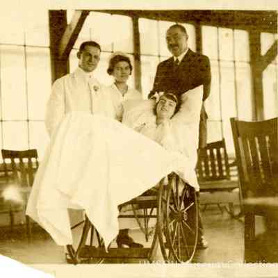 Patient in a wheelchair attended by a physician, nurse, and family member, University Hospital ca. 1920