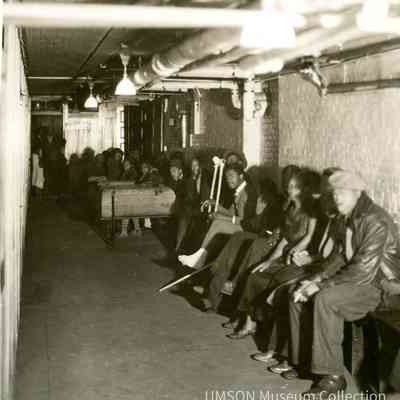 Black patients sitting on wooden benches in a basement hallway, segregated outpatient clinic, University Hospital, Maryland, 1934