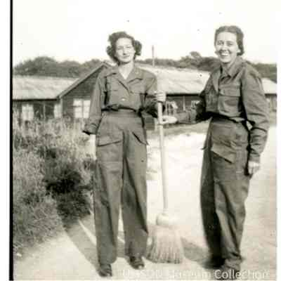 Nurses with a broom outside wooden barracks in England, 1944