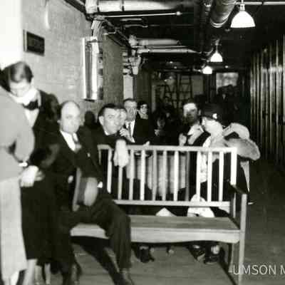 White patients sitting on wooden benches in a basement hallway, segregated outpatient clinic, University Hospital, Maryland, 1934