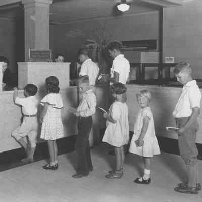 Schoolchildren stand in line at a bank