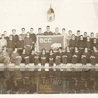 Group of swimmers by pool holding banner with "BCC" and image of a bear