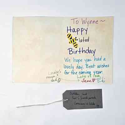 An opened belated birthday card to Wynne from Jane and Edi. The "B" of Belated is stylised as a Bee. With a brown, handwritten luggage tag.