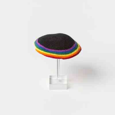 A rainbow knitted Kippah on a clear hat stand.