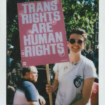 A person smiling and holding a sign which says "Trans Rights Are Human Rights".