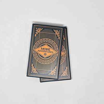 Small green box of cards with gold foil design reading "MORE ADVENTURES" inside a diamond.