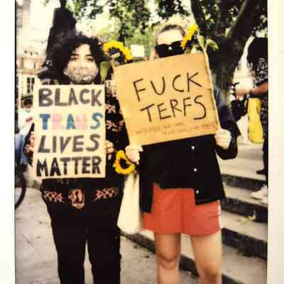Two individuals stand outdoors holding protest signs advocating for Black trans rights and opposing TERFs.