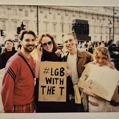 A group of people at a protest hold signs which say phrases such as "#LGB WITH THE T".