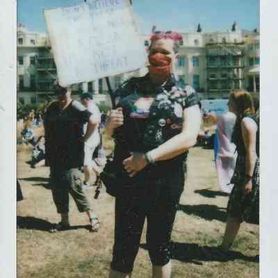 A person with pink hair holds a sign which has a message that is too blurry to make out.