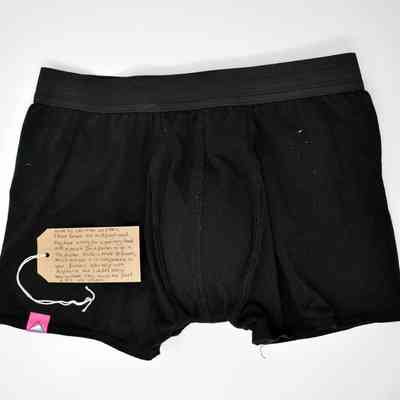 Pair of black Spectrum Outfitters boxer shorts, with a small pink log on the leg hem. With a brown, handwritten luggage tag.