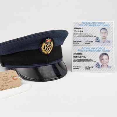 A blue RAF police cap sits beside two police warrant cards, featuring photographs and identifying details.