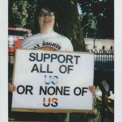 A person is holding a sign that says, "Support all of us or none of us."