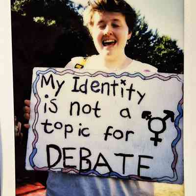 A person holds a sign reading "My Identity is not a topic for DEBATE".
