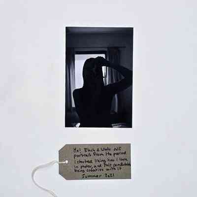 A black and white photo self-portrait/silhouette photo taken in a mirror. With a brown, handwritten luggage tag.