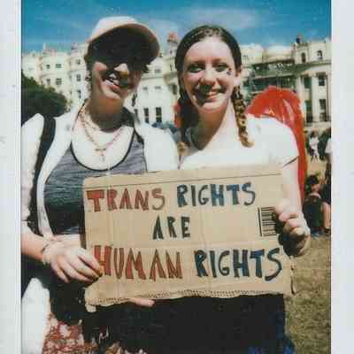 Two smiling individuals stand outdoors holding a sign that reads "Trans rights are human rights."