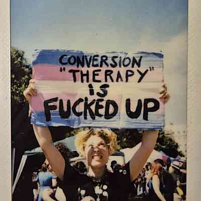 A person holds a sign which says "CONVERSION THERAPY IS FUCKED UP".
