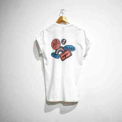 A white t-shirt with colorful illustrations and positive messages hangs on a wooden hanger.