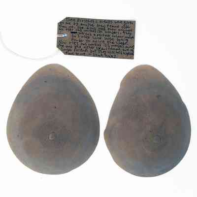 A pair of teardrop shaped breast forms, slightly discolored. With a brown hand written luggage tag.