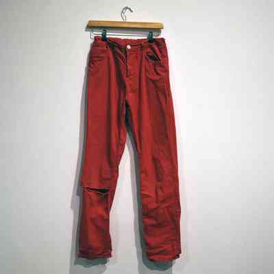 A pair of red pants is hanging on a wooden hanger against a plain wall.