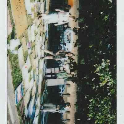 The image shows people standing near a fence with lots of placards laid on the ground beside them.
