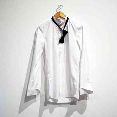 A formal, plain white, long sleeved shirt on a wooden hangar. A black bow tie hangs round the neck.