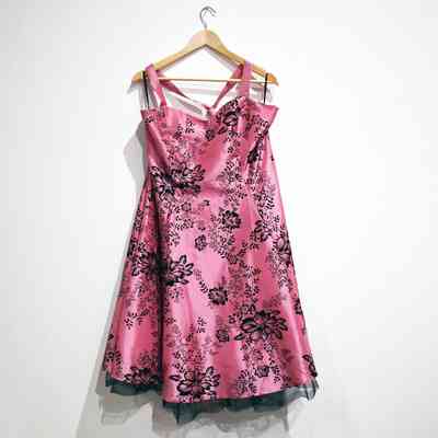 A pink dress with black floral patterns hangs on a wooden hanger against a white wall.