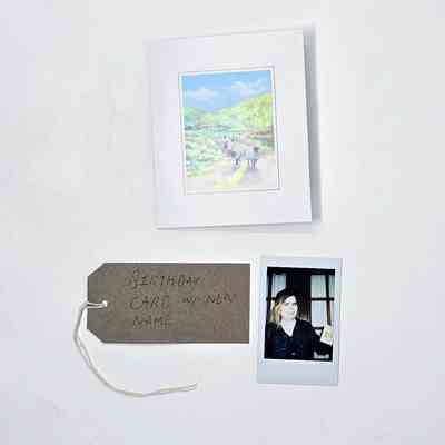 A birthday card with an illustration of sheep on a country lane. With a Polaroid and a brown, handwritten luggage tag.