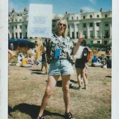A person holding a "Surf the Turf" sign poses joyfully in a sunny, crowded outdoor gathering.