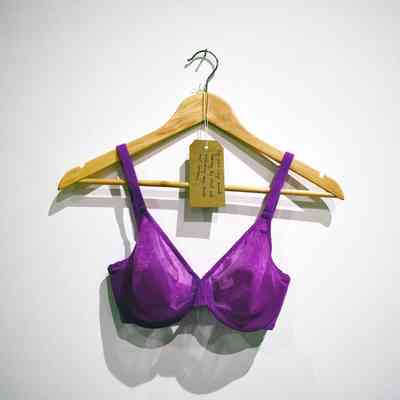 A fushia bink unpadded bra, with a glitter sheen to surface on a wooden hanger. Also, a brown, handwritten luggage tag.