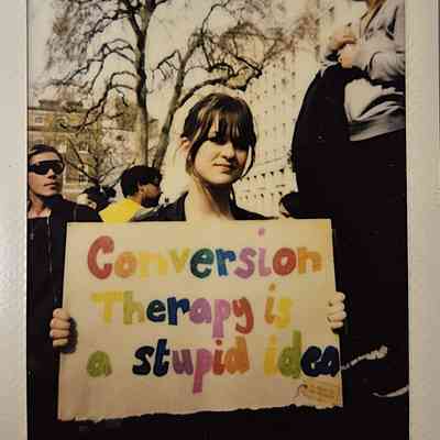 A person holds a colorful sign reading "Conversion Therapy is a stupid idea" during a protest.