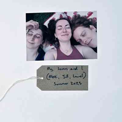 Close up photo of three peoples faces as they lie on the ground with their eyes closed. With a brown, handwritten luggage tag.